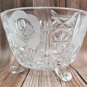 以下が含まれることがあります： 足付きの透明なガラスボウルで、エッチングされた花柄と幾何学模様が施されています。ボウルには側面にフロスト加工されたバラのデザインがあり、3つの湾曲した足で支えられています。ボウルは透明なガラス製で、ファセットパターンになっています。