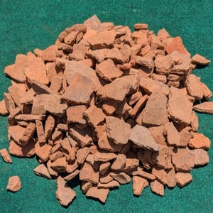 Peut inclure: Un grand tas d'éclats de terre cuite brisés présentant des formes irrégulières et des tailles variées. Les fragments présentent une couleur brun-rouge terreuse mate avec des textures poreuses rugueuses et des bords tranchants.