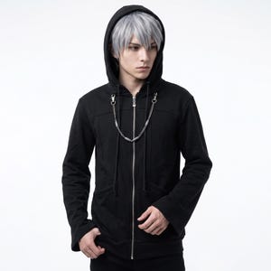 May include: A black zip-up hoodie featuring a silver-toned metal chain accessory attached to the collar area with lobster clasps. The garment includes a hood, long sleeves, and a central silver zipper closure, presenting a solid black fabric design.