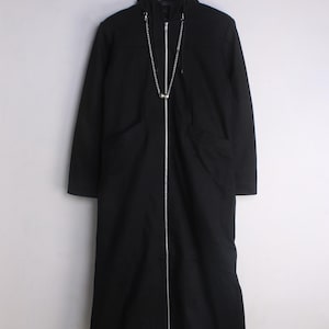 Peut inclure: Un manteau noir à capuche et manches longues doté d'une fermeture éclair argentée sur toute la longueur et d'une chaîne métallique argentée décorative drapée sur la poitrine. Le manteau possède deux poches latérales sur un cintre.