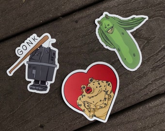 Puede incluir: Tres pegatinas con personajes de Star Wars. La primera pegatina es una ilustración en blanco y negro de un droide sosteniendo un bate de béisbol con la palabra "GONK" escrita en él. La segunda pegatina es un extraterrestre verde con una boca grande y una sonrisa de dientes. La tercera pegatina es una pegatina en forma de corazón con un fondo rojo y un extraterrestre amarillo con manchas negras dentro del corazón.