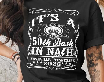 May include: Black t-shirt with white text that reads "IT'S A 50th Bash IN NASHVILLE, TENNESSEE 2026". The design includes two glasses of whiskey and decorative flourishes. The shirt is a crew neck.