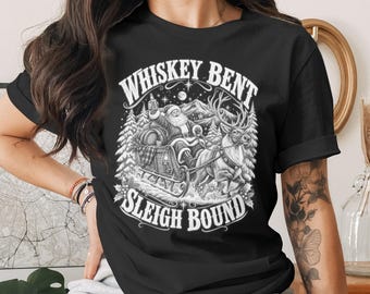 May include: A black short-sleeve t-shirt featuring a white graphic print of Santa Claus riding in a sleigh pulled by a reindeer. The text "WHISKEY BENT" is arched above the illustration, and "SLEIGH BOUND" is printed in a banner below the design.