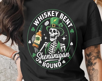 May include: Black t-shirt with a green and white graphic. The graphic features a skeleton wearing a green hat and holding a whiskey bottle. Text reads "Whiskey Bent, Shenanigan Bound."