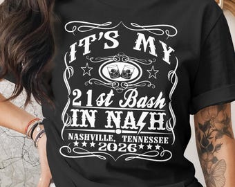 May include: Black t-shirt with white text that reads "IT'S MY 21st Bash IN NAZH" with "Nashville, Tennessee 2026" below. The design includes stars and images of two glasses of whiskey.
