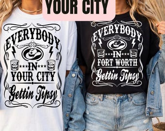 May include: Two t-shirts, one white and one black, with a graphic design. The design includes the text "EVERYBODY IN YOUR CITY Gettin Tipsy" and "EVERYBODY IN FORT WORTH Gettin Tipsy". The design features a cowboy hat, lightning bolts, and whiskey glasses.