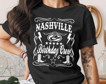 May include: A black short-sleeved t-shirt featuring white graphic text that reads Nashville Birthday Crew. The design includes a cowboy hat, two lightning bolts, five stars, a large star, and two cowboy boots, all framed by decorative swirls.