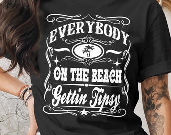 May include: Black t-shirt with white text that reads "EVERYBODY ON THE BEACH Gettin Tipsy." The design includes a palm tree graphic and decorative flourishes. The shirt is a casual wear item.
