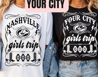 May include: Two t-shirts, one white and one black, with a graphic design. The white shirt says "Nashville girls trip" and the black shirt says "Your City girls trip". Both shirts have a cowboy hat and boot design.