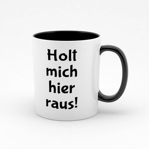 Könnte beinhalten: Weiße Keramiktasse mit schwarzem Rand und Henkel. Die Tasse hat einen schwarzen Schriftzug mit der Aufschrift "Holt mich hier raus!"