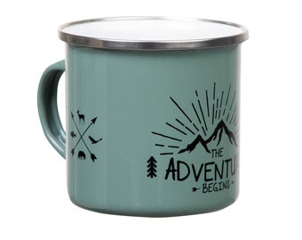 Może przedstawiać: Zielony kubek kempingowy z emalii z białym rantem i czarnym nadrukiem z napisem "The Adventure Begins" z górami i wzorem promieni słońca.