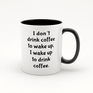 Könnte beinhalten: Eine weiße Kaffeetasse mit schwarzem Henkel und schwarzem Rand. Die Tasse hat einen schwarzen Text mit der Aufschrift "Ich trinke keinen Kaffee, um aufzuwachen, ich wache auf, um Kaffee zu trinken."