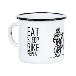 Può includere: Tazza in smalto bianco con bordo nero e una grafica in bianco e nero di una persona che guida una mountain bike. Il testo "EAT SLEEP BIKE REPEAT" è stampato sulla tazza.