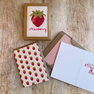 May include: A framed card with a red strawberry illustration and the word "strawberry" in pink script. A matching card with a strawberry pattern and an open card with text are also visible.