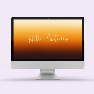 May include: A silver desktop computer with a screen displaying a gradient of orange and brown hues. The words "Hello Autumn" are written in a cursive font across the screen. The computer is set against a light purple background.