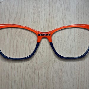 May include: Orange and blue cat-eye glasses with the word "BEARS" printed on the bridge.