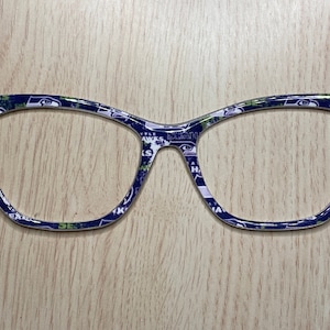 May include: A pair of cat-eye glasses with a white frame and a blue and green pattern featuring the Seattle Seahawks logo.