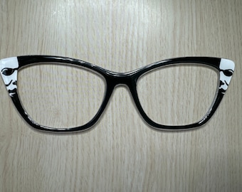 Peut inclure: Lunettes de soleil noires de forme œil de chat avec des motifs blancs sur les côtés.