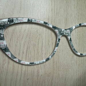 May include: A pair of cat-themed eyeglasses with a white frame and a black and white cat print. The glasses have a cat-eye shape.