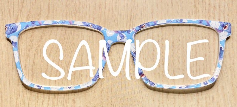 Puede incluir: Montura de gafas con un patr&oacute;n azul claro de peque&ntilde;os personajes de dibujos animados y la palabra SAMPLE impresa en letras blancas grandes en el centro. La montura tiene forma rectangular con esquinas redondeadas y acabado liso.