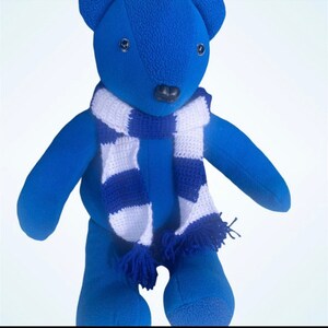 May include: A blue plush teddy bear wearing a white and blue striped scarf. The bear has black eyes and a black nose.