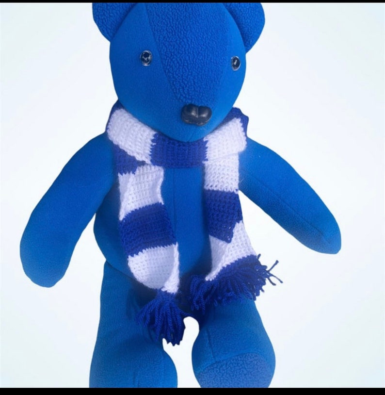 May include: A blue plush teddy bear wearing a white and blue striped scarf. The bear has black eyes and a black nose.