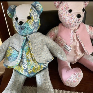 May include: Two handmade teddy bears, one with a blue and green floral pattern and a grey geometric jacket, the other with a pink and floral pattern and a pink waistcoat. Both bears have black eyes and a white nose. The bear with the pink waistcoat has a tag that reads "Made with love by Christine".