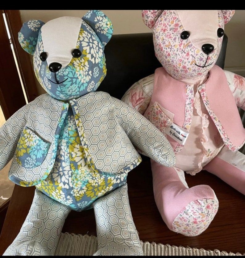 May include: Two handmade teddy bears, one with a blue and green floral pattern and a grey geometric jacket, the other with a pink and floral pattern and a pink waistcoat. Both bears have black eyes and a white nose. The bear with the pink waistcoat has a tag that reads "Made with love by Christine".