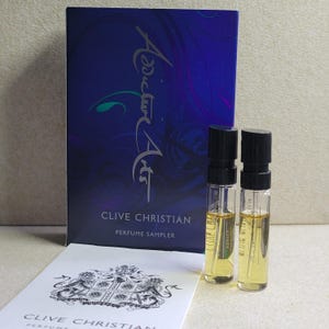 May include: A Clive Christian perfume sampler box with the text "Addict Art" and "Clive Christian Perfume Sampler". The box contains two small glass vials of perfume.