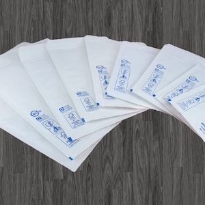 Op de afbeelding: Een groep witte gevoerde enveloppen met blauwe bedrukte instructies en een barcode. De enveloppen zijn in een waaier op een houten oppervlak gerangschikt.