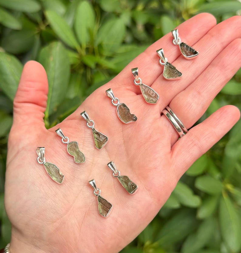May include: Eight small, irregular, olive-green textured stone pendants, each set in a polished silver-toned metal bail. The pendants vary slightly in shape and size, displaying a rough, natural surface texture characteristic of raw mineral specimens.