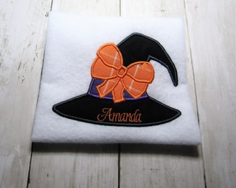 May include: White fabric with an embroidered black witch hat with an orange bow and the name "Amanda" in cursive.