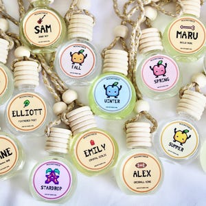 May include: A collection of small, clear glass bottles with wooden tops and decorative labels. Each bottle has a different name and a cartoon graphic, such as "Fall" with a pumpkin or "Summer" with a lemon. The bottles are connected by a rope.