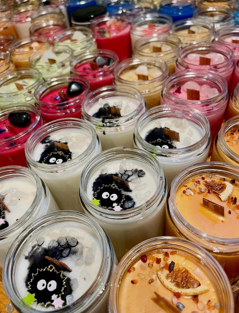 Puede incluir: Una colecci&oacute;n de velas perfumadas en frascos de vidrio transparente. Las velas presentan diferentes colores, incluyendo rosa, rojo y naranja, con elementos decorativos como cristales y mechas de madera. Algunas velas tienen un dise&ntilde;o de personaje de dibujos animados.