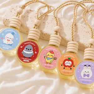 Könnte beinhalten: Fünf Auto-Lufterfrischer mit Cartoon-Charakter-Designs. Jede runde Glasflasche hat einen Holzverschluss und eine geflochtene Kordel zum Aufhängen. Die Etiketten zeigen einen Schneemann, einen Vogel, ein Küken, einen Apfel und ein Kaninchen.