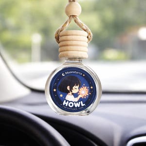 May include: A car air freshener with a round glass bottle and wooden top, hanging from a rearview mirror. The bottle features a blue label with an anime-style illustration and the text "HOWL CAR DIFFUSER".