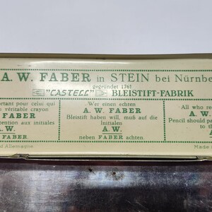 May include: A rectangular metal pencil tin with a cream-colored lid featuring green text and graphics. The lid displays the A.W. Faber brand name, the text "CASTELL" BLEISTIFT-FABRIK, and instructions in French, German, and English regarding the initials A.W.