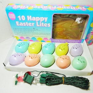 Puede incluir: Una caja de 10 Happy Easter Lites, una cadena de luces en forma de huevo de color pastel con un cable verde. La caja es azul y blanca con una imagen de las luces en el interior. Las luces están iluminadas por 10 bombillas reemplazables en miniatura. Completo con cable y lámpara de 12V.