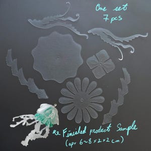 Puede incluir: Un conjunto de siete piezas transparentes de manualidades con temática floral, que incluyen una margarita, una flor de cuatro pétalos y varias formas de hojas y espirales. El texto "One set 7 pcs" y "Re Finished product Sample (aprox. 6~8 x 2 x 2 cm)" está escrito en tinta turquesa.