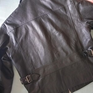 Pu&ograve; includere: Giacca in pelle marrone scuro dal design classico. La giacca presenta un colletto a revers, una chiusura con cerniera e due cinturini regolabili con fibbia in vita. La pelle ha un aspetto leggermente invecchiato.