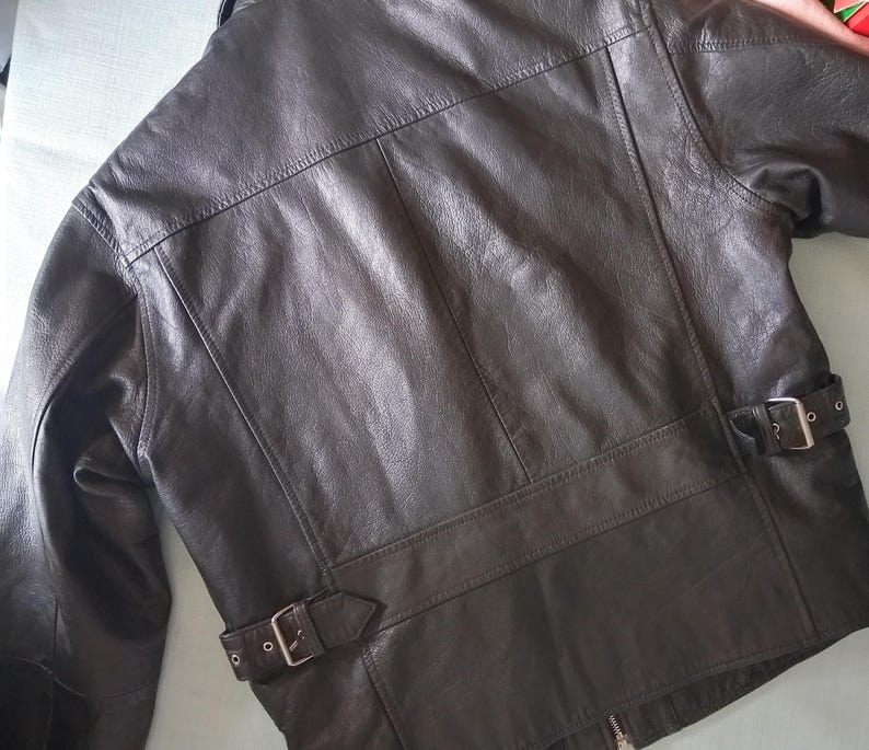 Pu&ograve; includere: Giacca in pelle marrone scuro dal design classico. La giacca presenta un colletto a revers, una chiusura con cerniera e due cinturini regolabili con fibbia in vita. La pelle ha un aspetto leggermente invecchiato.