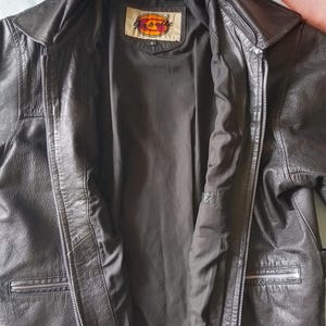 Pu&ograve; includere: Giacca in pelle nera con chiusura a zip e due tasche anteriori. La giacca ha un collo e un'etichetta all'interno del colletto. La giacca &egrave; aperta, rivelando una fodera scura.