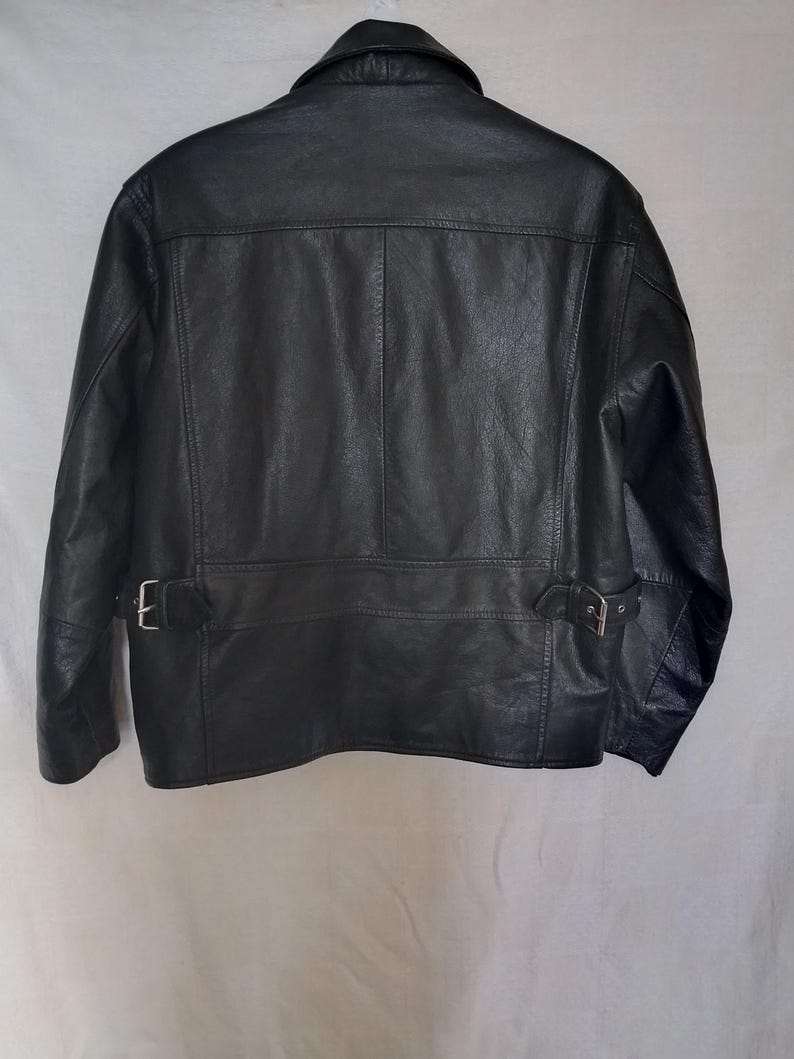 Pu&ograve; includere: Giacca in pelle nera con colletto, cuciture a vista e due cinturini regolabili con fibbia in vita. La giacca ha un design classico e un aspetto strutturato.