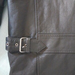 Pu&ograve; includere: Primo piano di una giacca in pelle nera con chiusura a fibbia. La giacca ha una superficie strutturata e dettagli di cucitura visibili. La fibbia &egrave; color argento.
