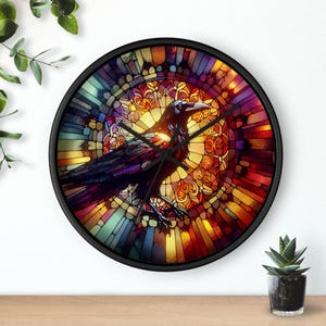 May include: A black clock with a stained glass design featuring a raven in a colourful circular pattern. The clock face is surrounded by a black frame.