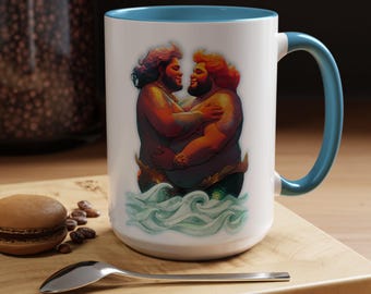 Puede incluir: Una taza de cerámica blanca con un borde y un asa azules. La taza presenta una ilustración colorida de dos tritones abrazándose en el océano.
