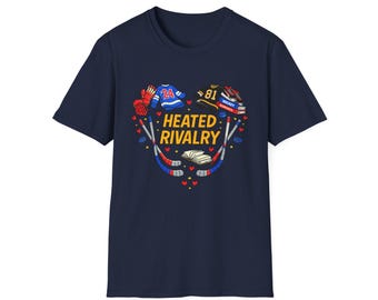 May include: Navy blue t-shirt with a heart-shaped graphic featuring hockey jerseys, gloves, and sticks. The graphic includes the text "Heated Rivalry" in yellow. The design incorporates red, blue, and white colors, with small red hearts.