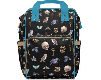 May include: A black backpack with a blue trim and a repeating pattern of skulls, owls, keys, mushrooms, and other woodland creatures.