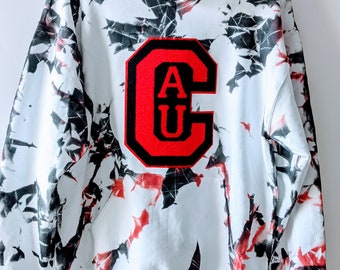 Może przedstawiać: Biała bluza z kapturem z czarno-czerwonym wzorem tie-dye. Bluza ma dużą czerwoną naszywkę "AU" z przodu.