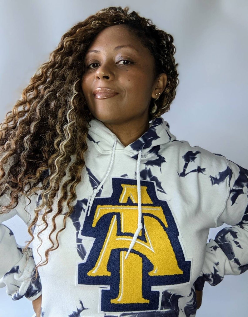 May include: A white tie-dye hoodie with a large navy blue and gold embroidered letter "A" on the front.